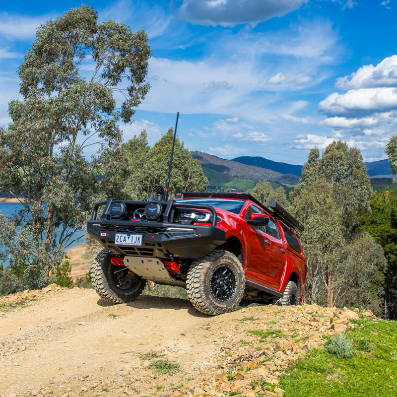 ARB equipped Mazda BT-50 climbing a rocky off road track with visible wheel articulation, overlooking a lake and mountain landscape.