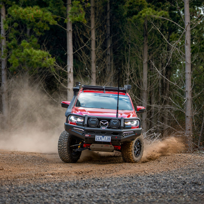 Front view of an ARB equipped Mazda BT-50 driving along a gravel forest track with dust trailing behind the vehicle.