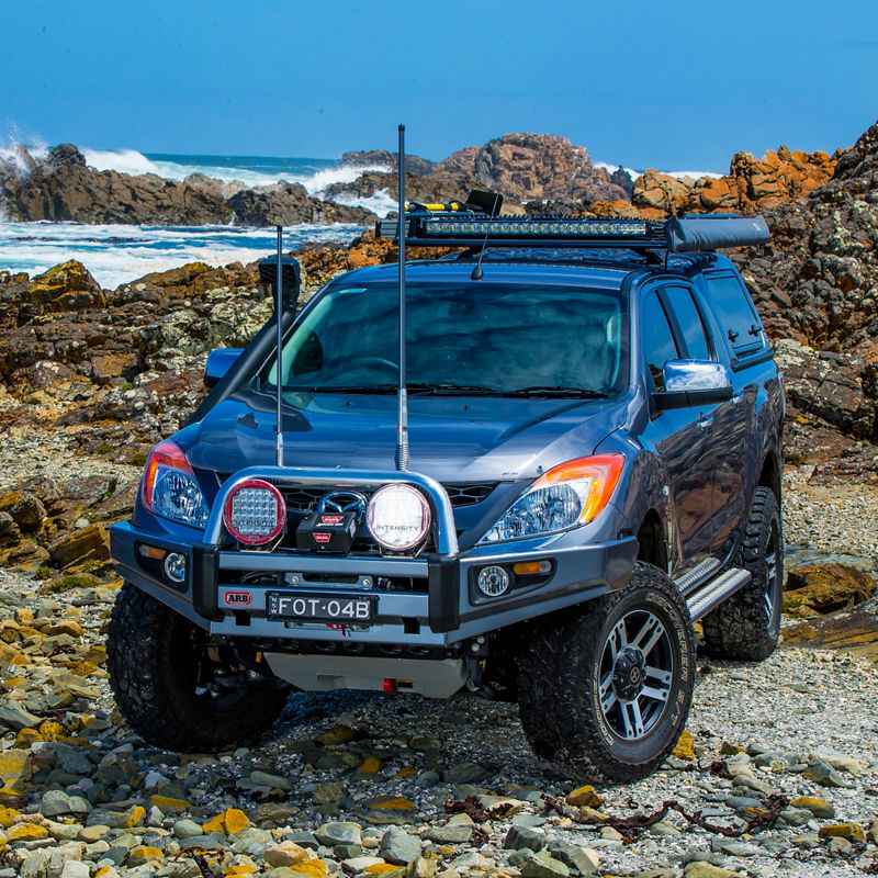 ARB equipped Mazda BT-50 parked on a rocky coastal shoreline with a bull bar, driving lights, canopy and roof rack system.