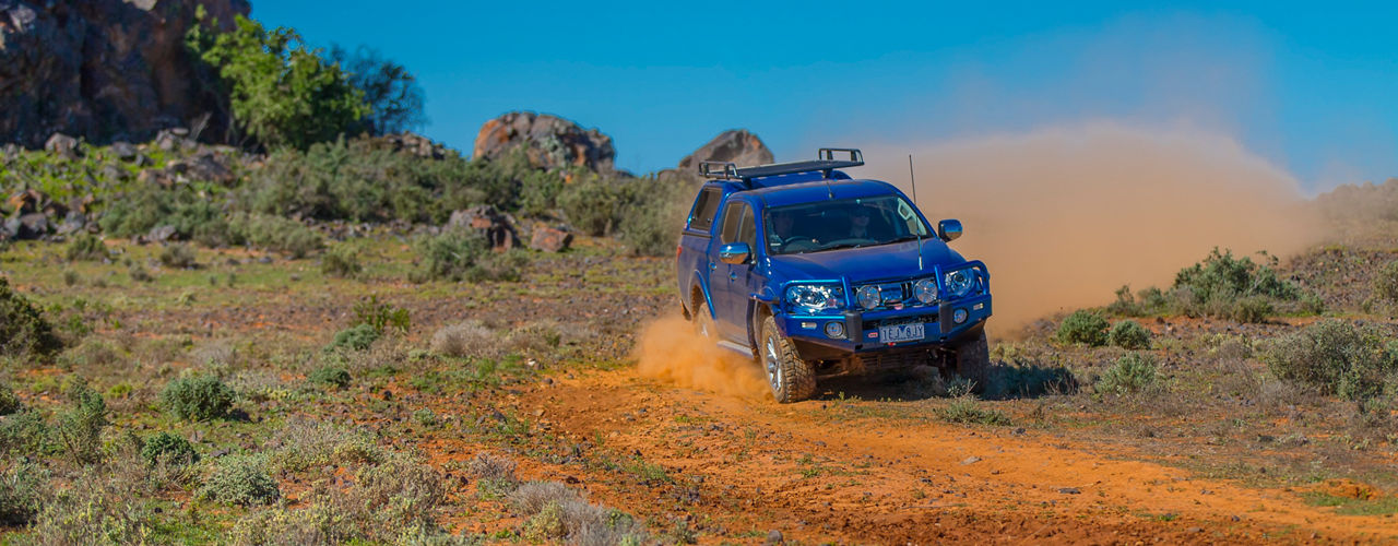 Mitsubishi Triton driving on a dusty outback track with an ARB bull bar, canopy and roof rack system.