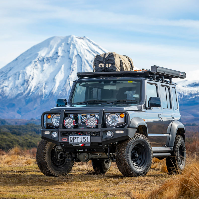 ARB equipped Suzuki Jimny fitted with a roof rack system and awning, parked in front of a snow covered mountain.