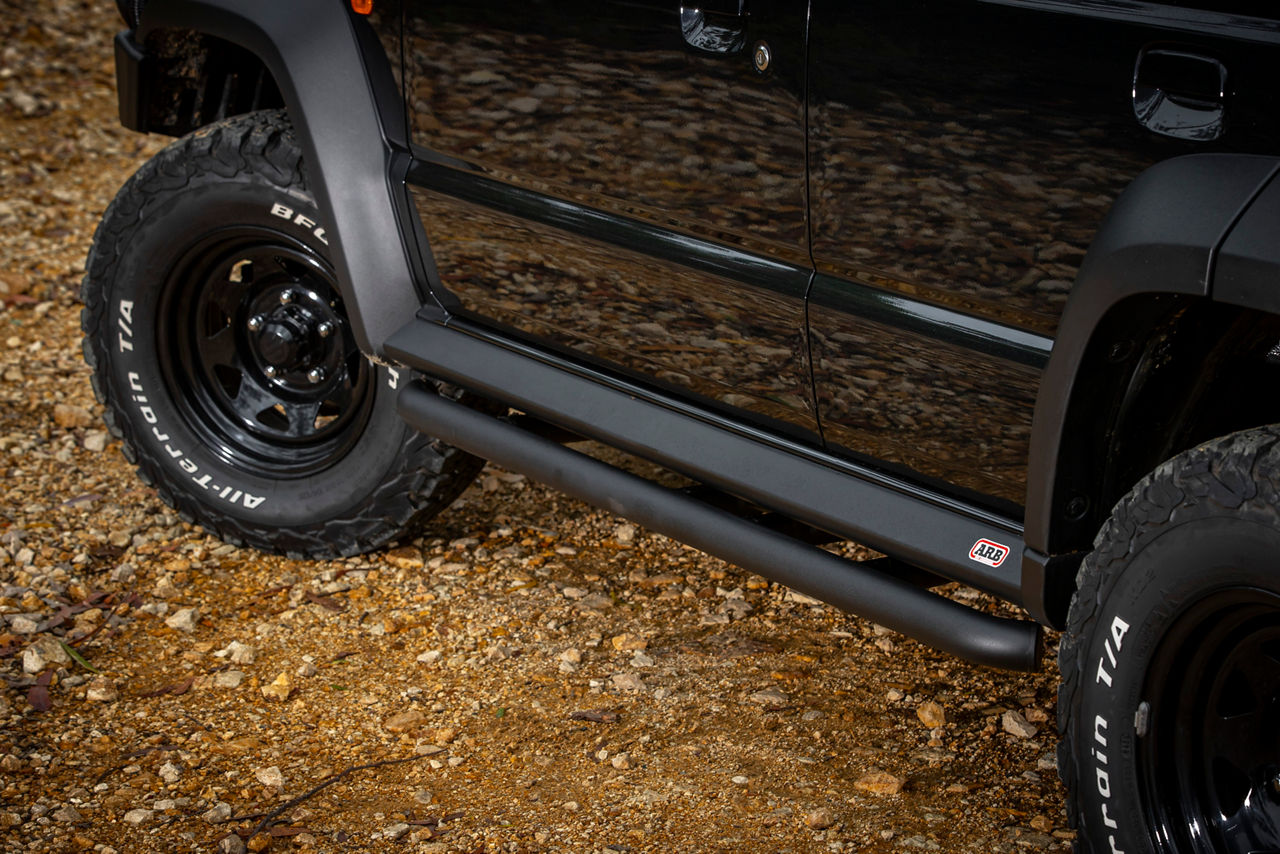 Close-up view of an ARB rock slider fitted to a Suzuki Jimny on rocky terrain.