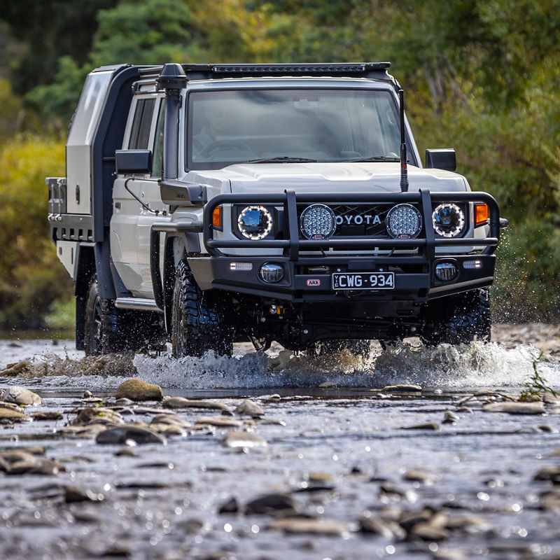 Front view of a Toyota LandCruiser 79 Series crossing a rocky creek, fitted with an ARB bull bar, driving lights, snorkel and canopy.