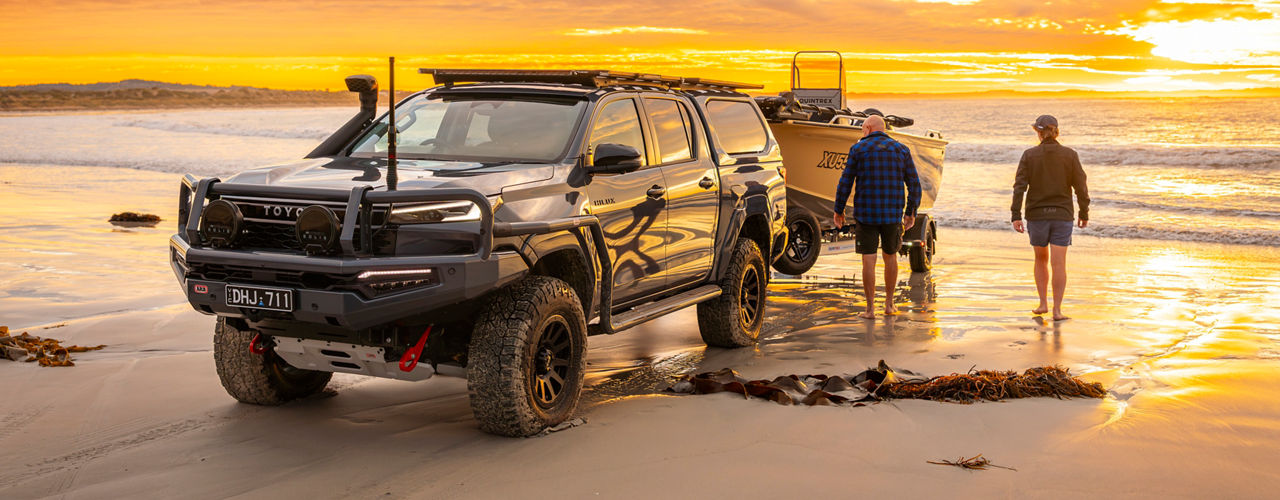 Copilot said:  ARB equipped Toyota HiLux 26 towing a boat on a beach at sunset.