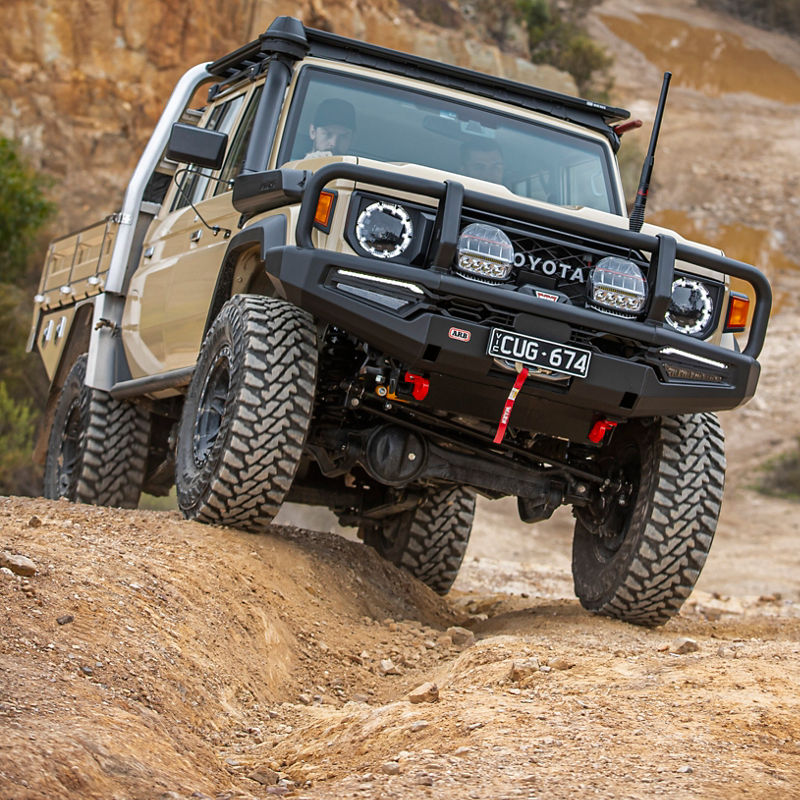 Toyota LandCruiser 79 Series fitted with an ARB bull bar, driving lights and roof rack system navigating a rocky off road track with visible wheel articulation.