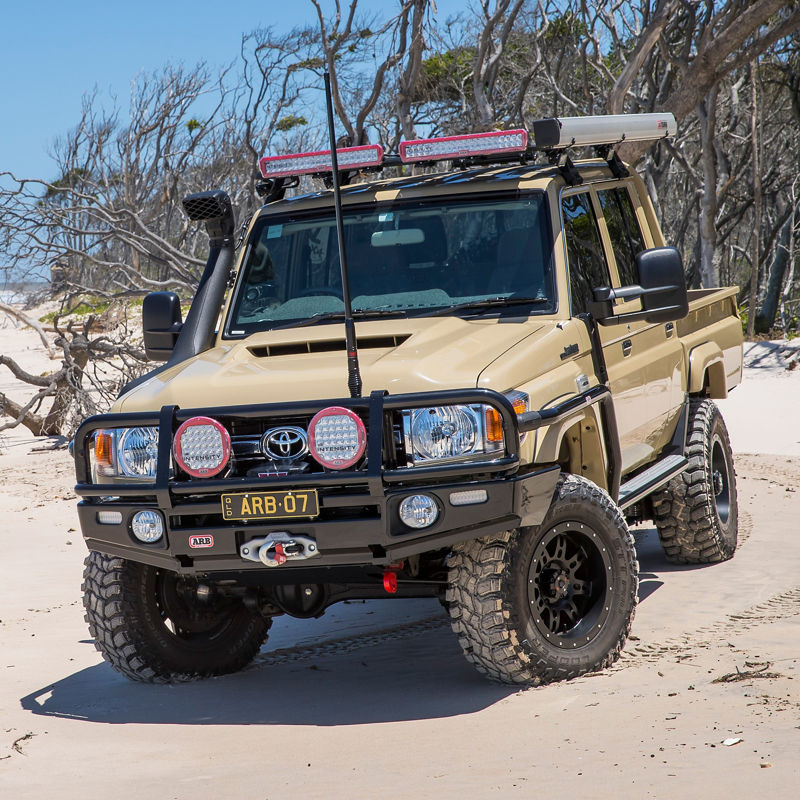 Toyota LandCruiser 79 Series fitted with an ARB bull bar, Intensity driving lights, snorkel, roof rack system, awning and winch, parked on a sandy beach.