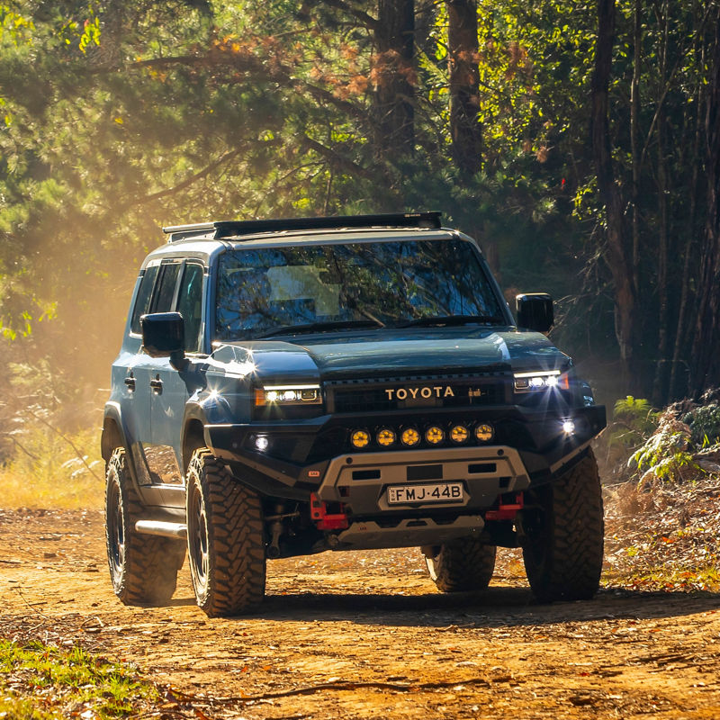 Toyota LandCruiser Prado 250 Series driving along a forest track, fitted with an ARB bull bar, driving lights, roof rack system and under vehicle protection.