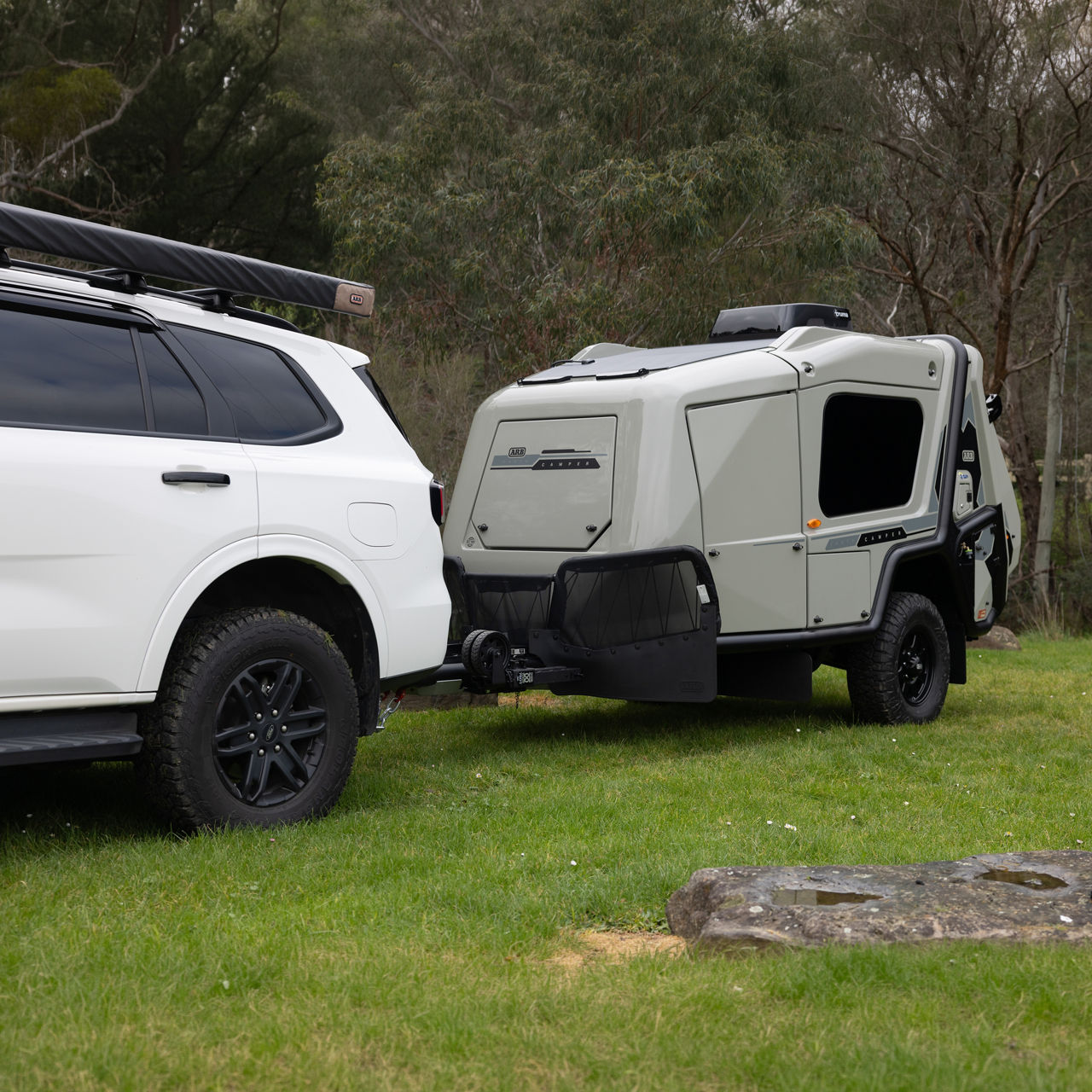 ARB Earth Camper GT being towed by a 4WD vehicle in a grassy campsite setting.