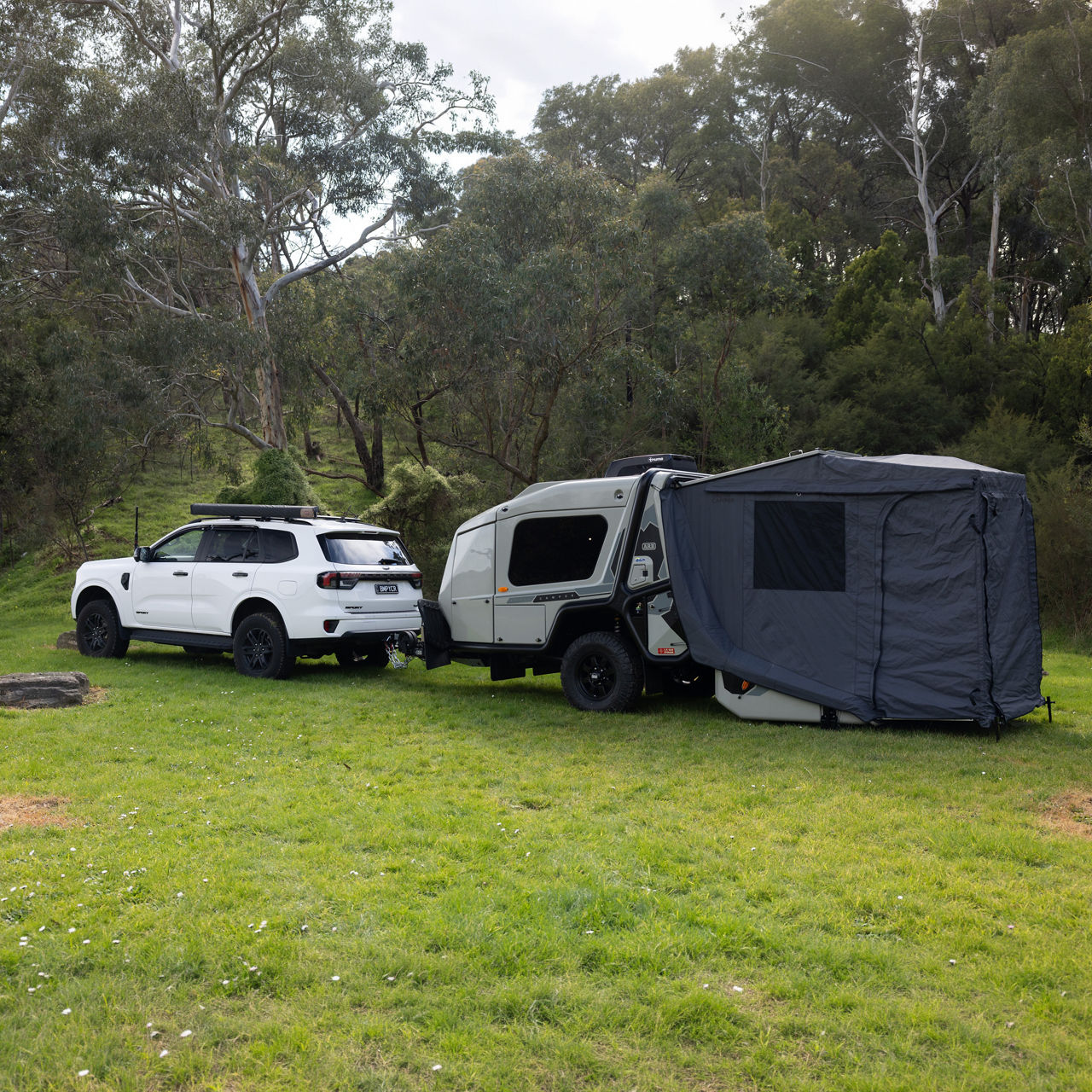 ARB Earth Camper GT with a fully deployed annex beside a 4WD vehicle at a grassy campsite.