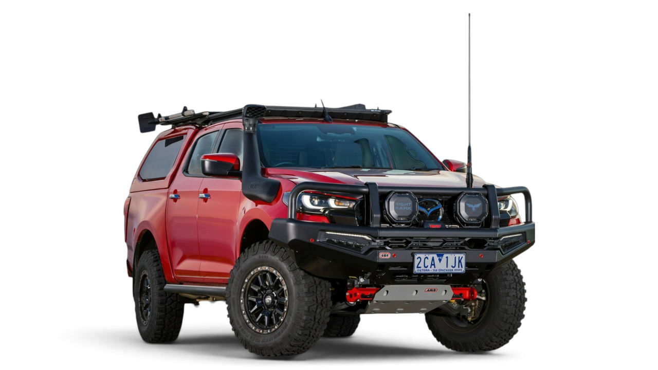 Front three quarter view of a Mazda BT-50 fitted with an ARB bull bar, driving lights, canopy and roof rack system on a white studio background.