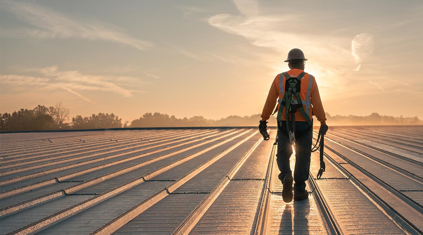 Builder walking across completed metal roof installation as the sun sets