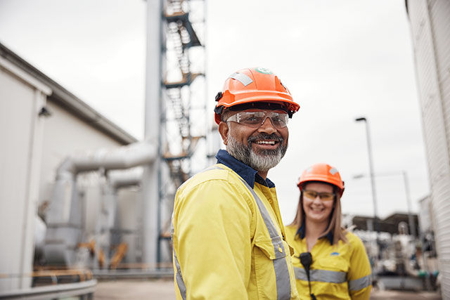 BlueScope workers smiling at the camera in an outdoor facility wearing protective gear