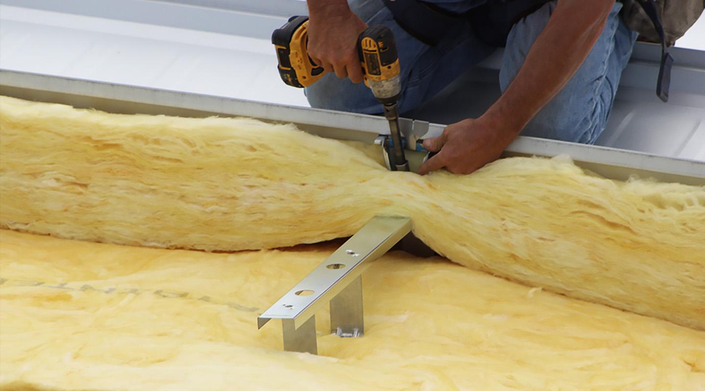 Close-up of insulation system installation, with fiberglass insulation being secured over metal supports on a steel roof assembly.
