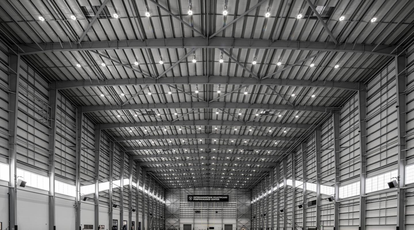 Interior view of a large steel building showcasing structural steel framing systems, with repeating rigid frames, exposed beams, and integrated wall panels creating a symmetrical, high-bay space.