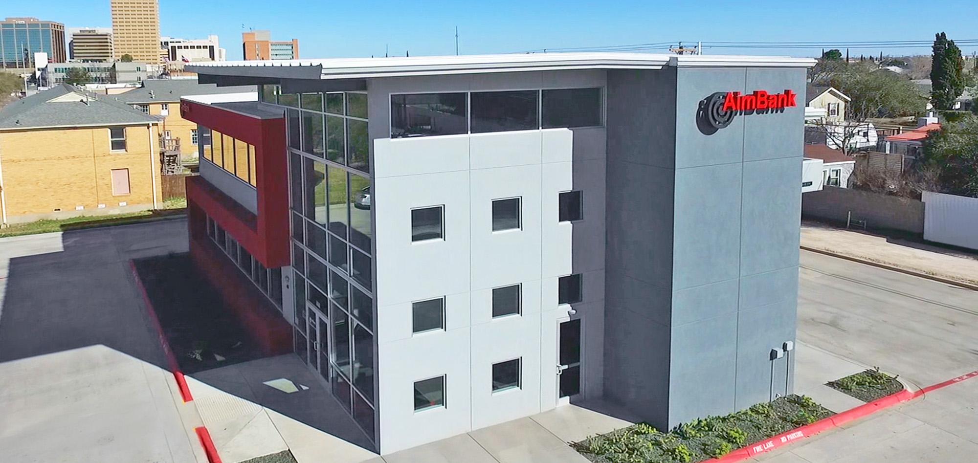 Modern multi-story office building with gray and white facade, expansive glass curtain wall and bold red architectural accents in an urban setting.