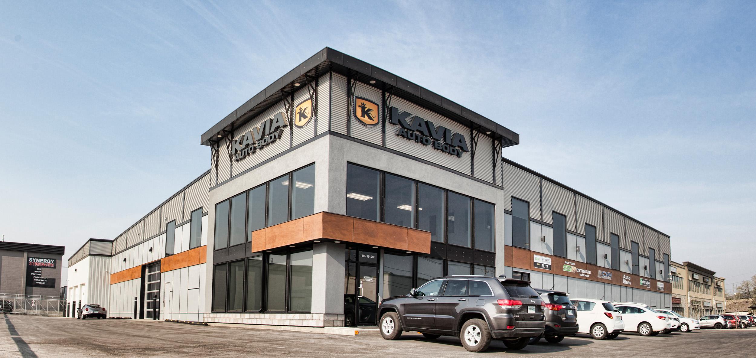Modern black-and-white industrial facility with expansive glass corner entry, warm wood-tone accents and bold geometric rooflines beneath a clear blue sky.