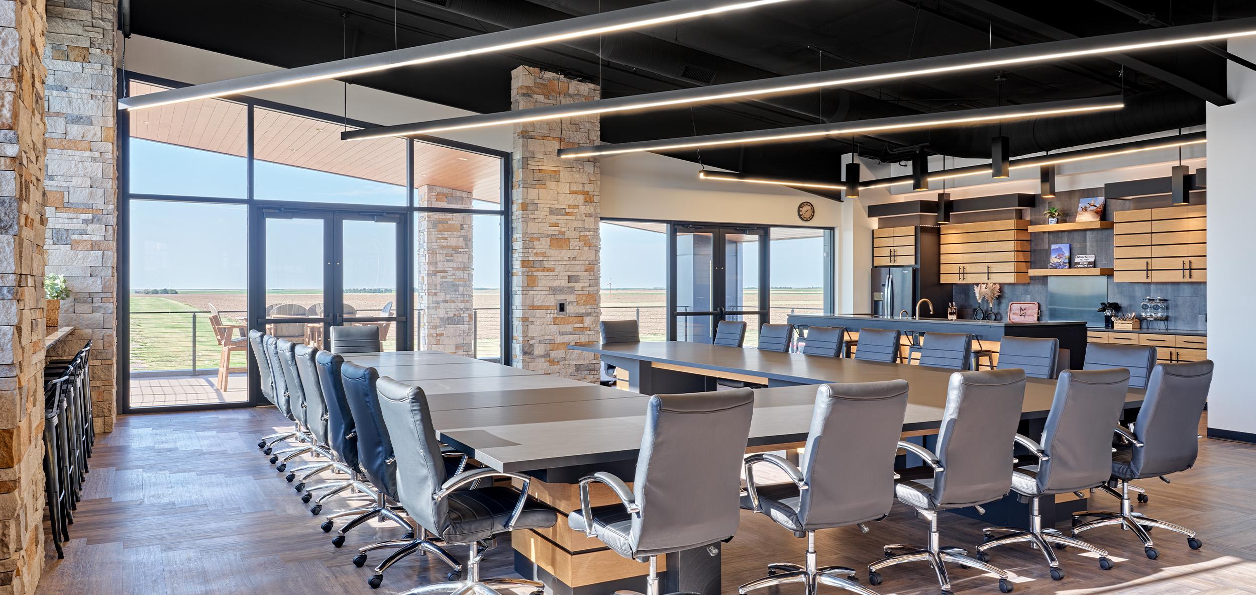 Modern conference space with long collaborative meeting table, floor-to-ceiling windows, stone accents and sleek linear lighting throughout.