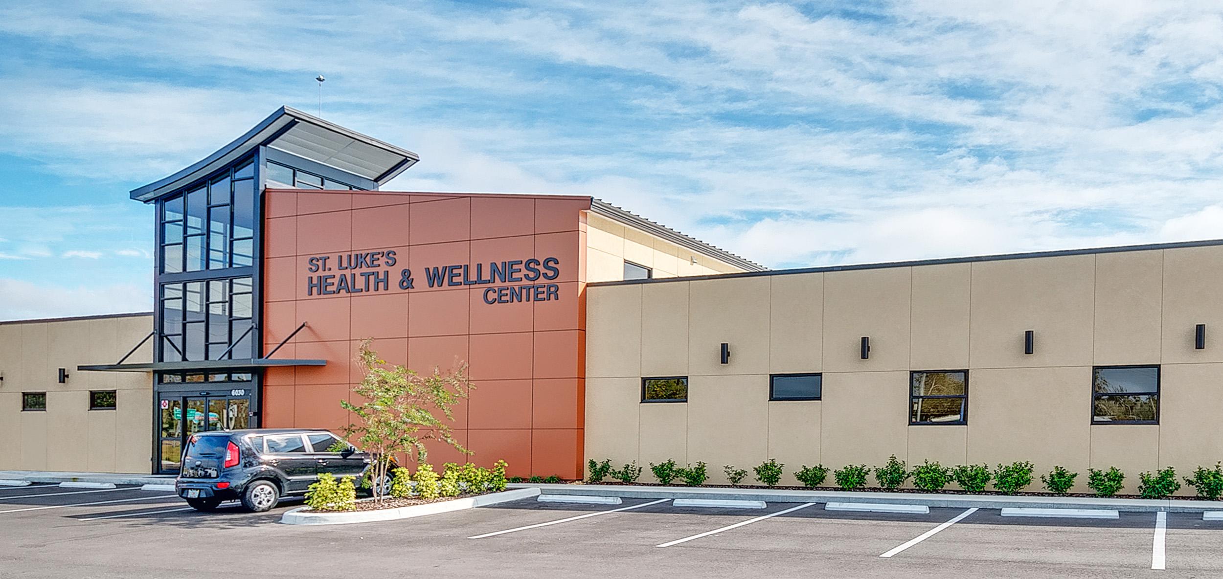 Modern healthcare and wellness facility with copper-toned entry feature, glass tower lobby and clean-lined facade beneath a bright blue sky.
