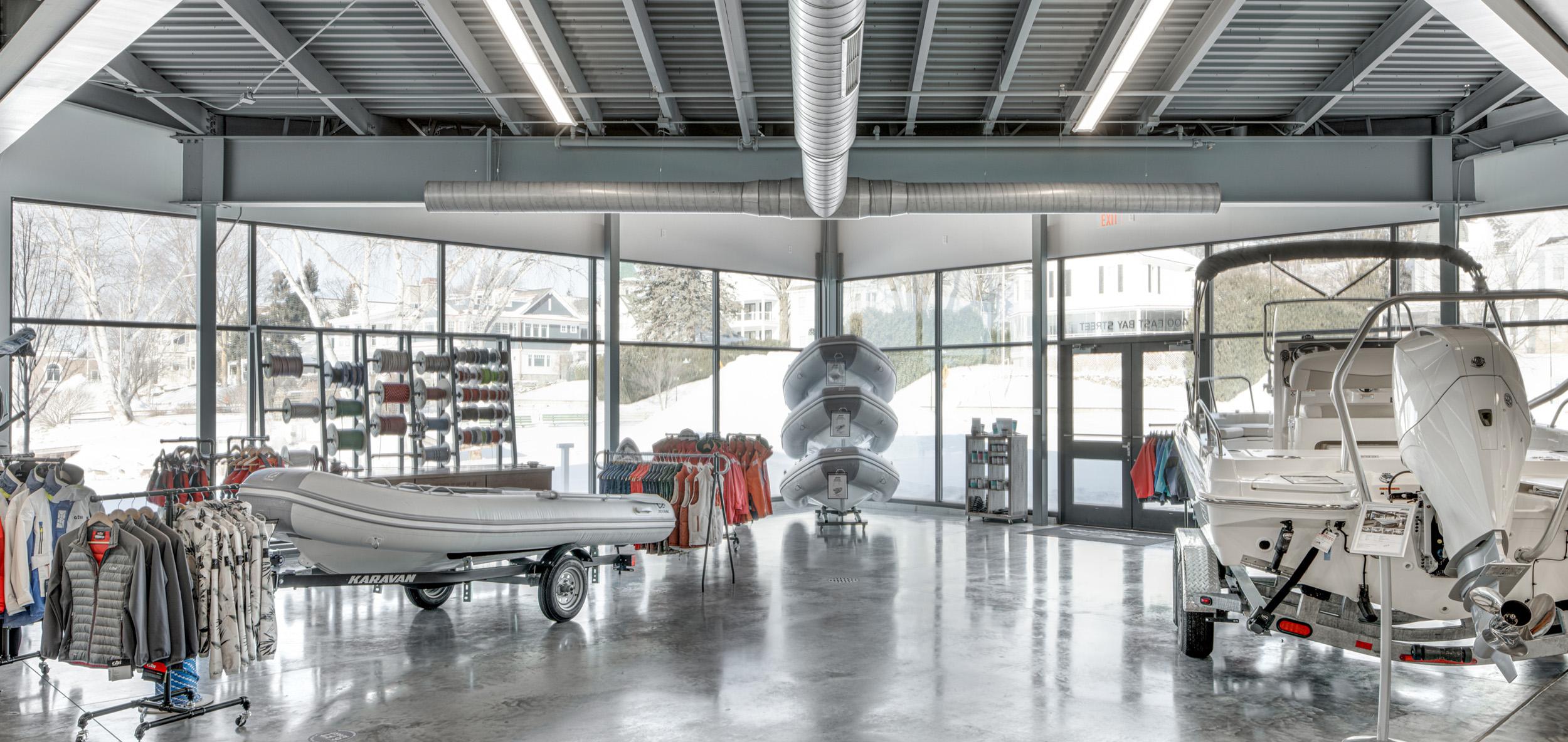 Bright marine showroom interior with exposed steel ceiling structure, polished concrete floors and large display windows showcasing boats and outdoor equipment.
