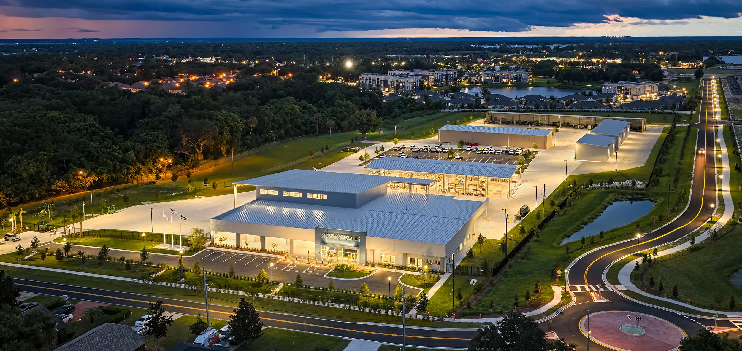 Aerial view of a modern energy and utilities facility with illuminated operations buildings, integrated infrastructure and surrounding road network at dusk.