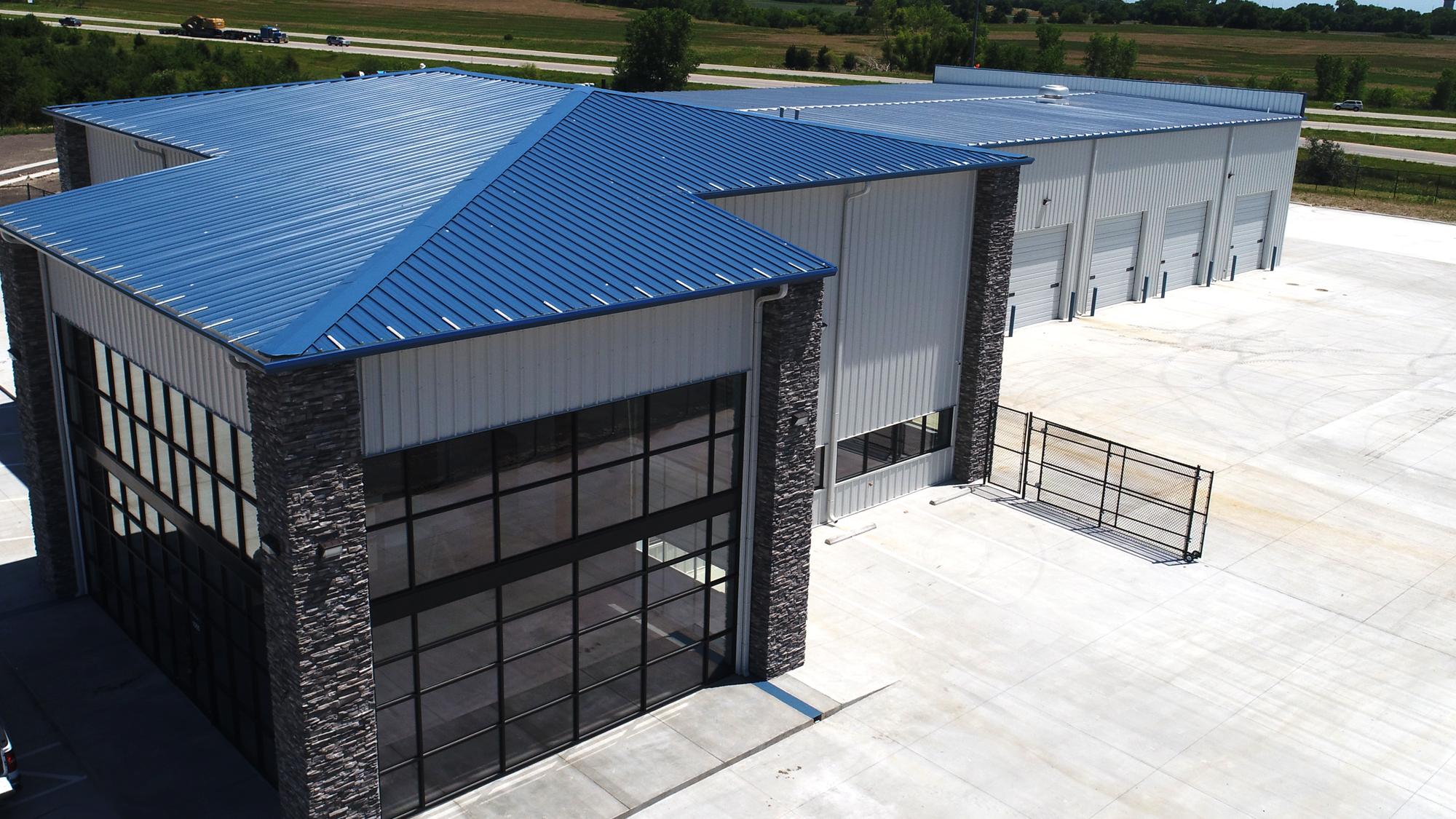Exterior view of the James Mason Enterprises facility featuring a blue metal roof, tall glass service bay doors and stone facade accents.