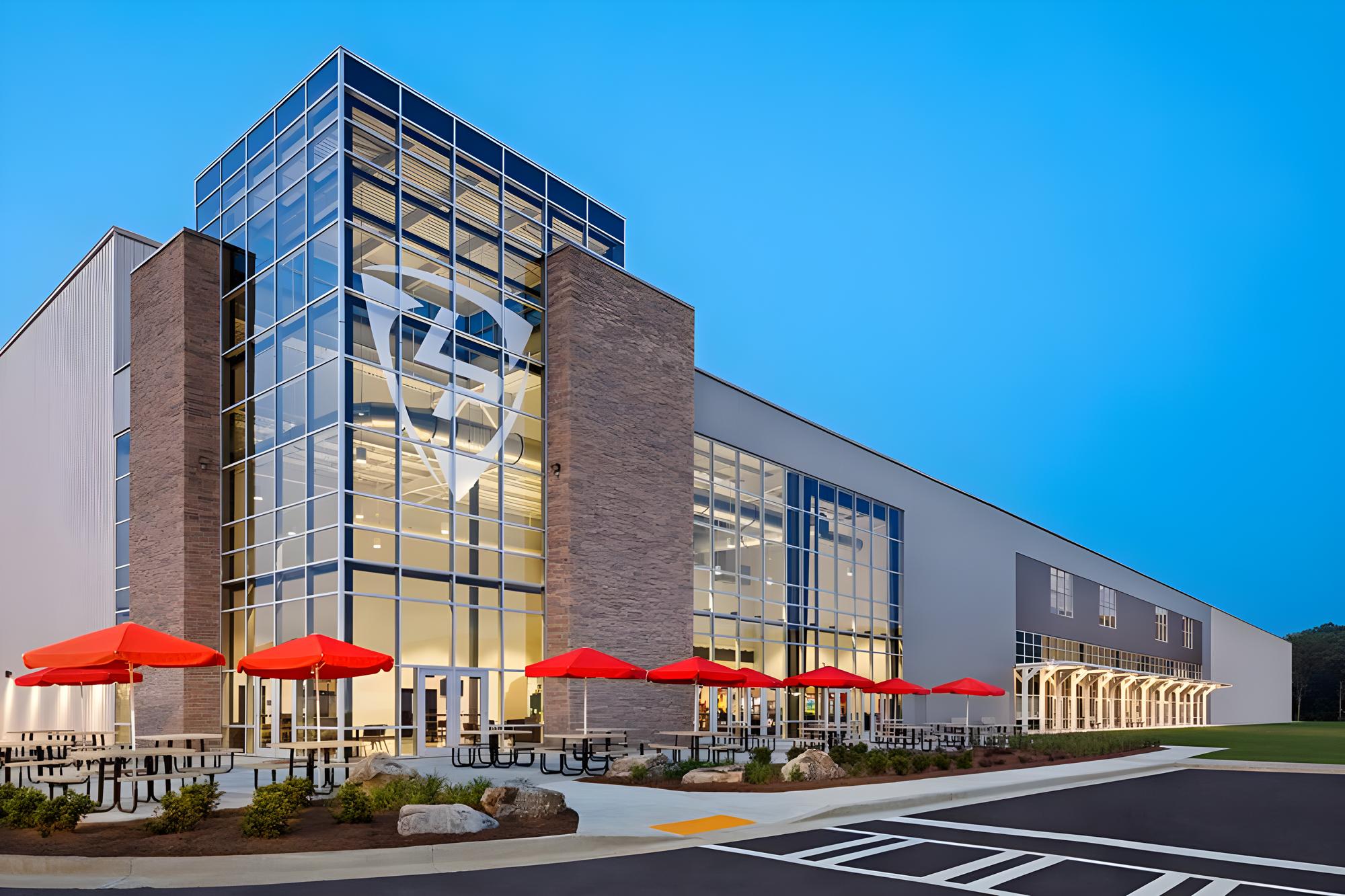 Evening exterior view of the LakePoint Sports Champions Center featuring a multi-story glass entrance, integrated outdoor gathering space and a large clear-span athletic facility designed for flexible year-round use.