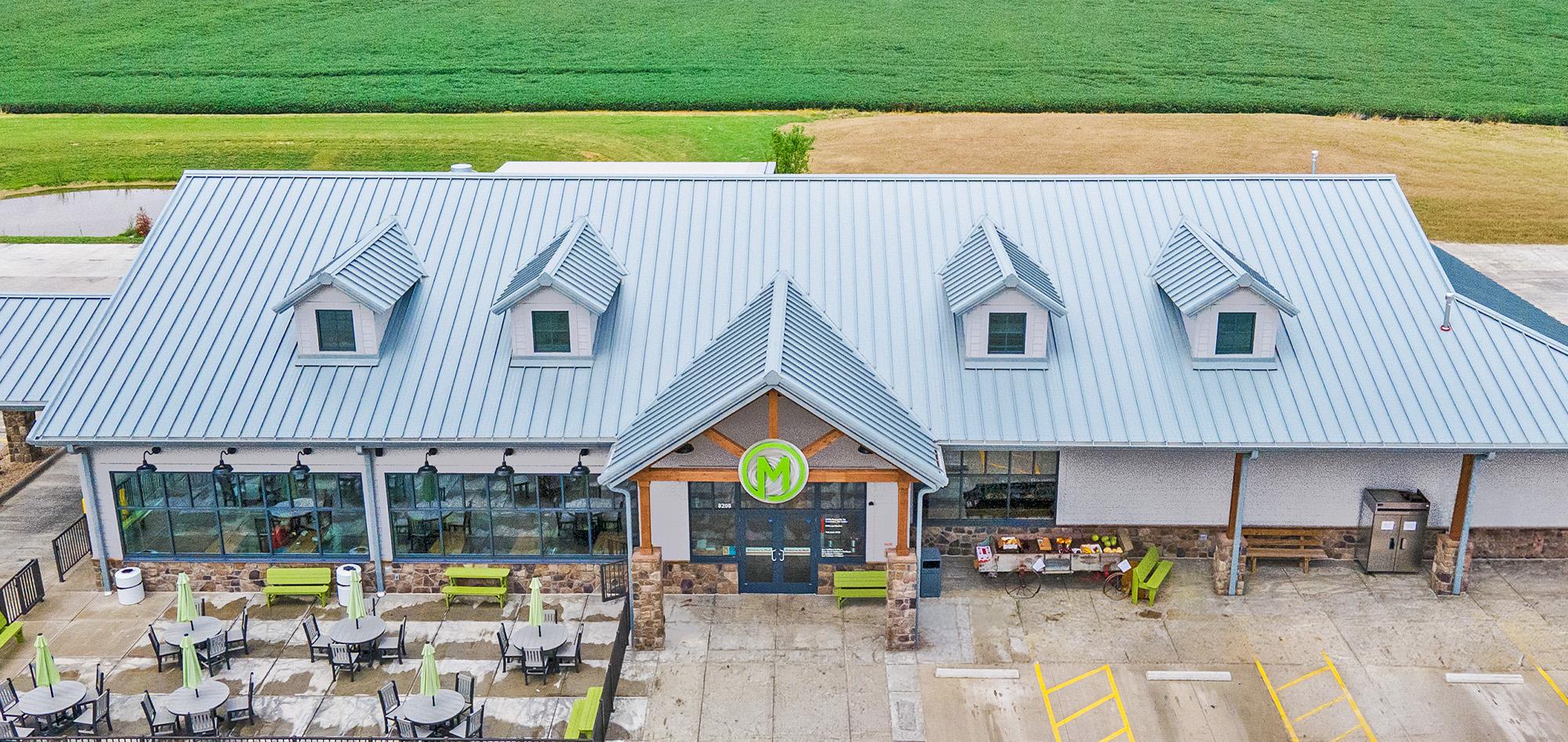 Retail market and gas station facility featuring standing seam metal roof system, covered outdoor seating and commercial steel building construction.