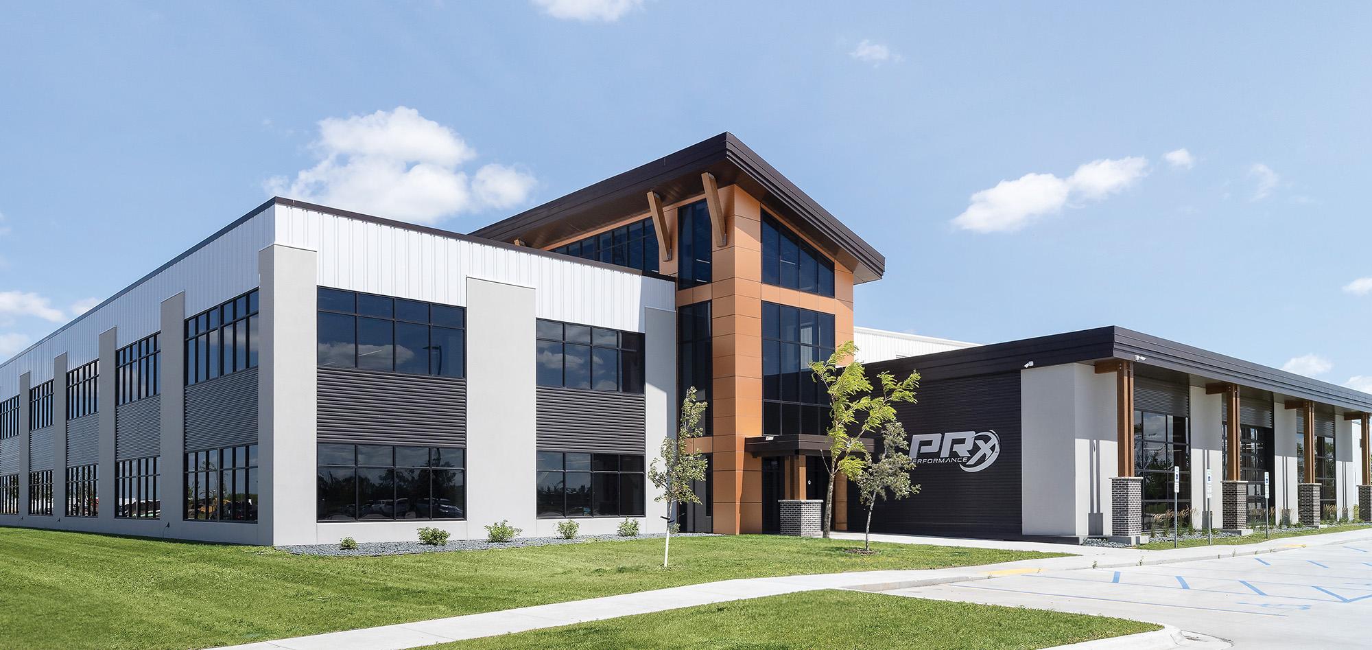 Contemporary corporate office building with a warm copper-toned entry tower, expansive glass frontage and landscaped green space beneath a bright blue sky.