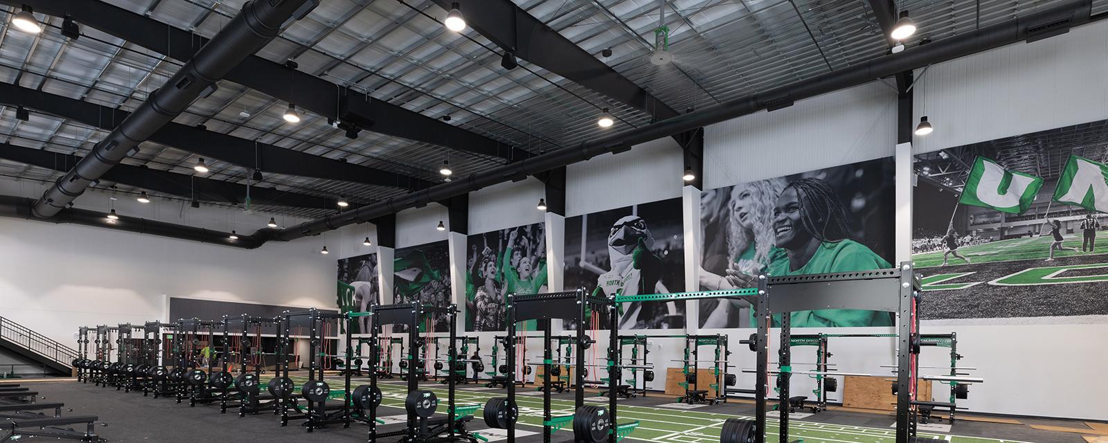 Modern athletic training facility with exposed steel framing, high-performance fitness equipment and large-scale sports graphics throughout an open training environment.
