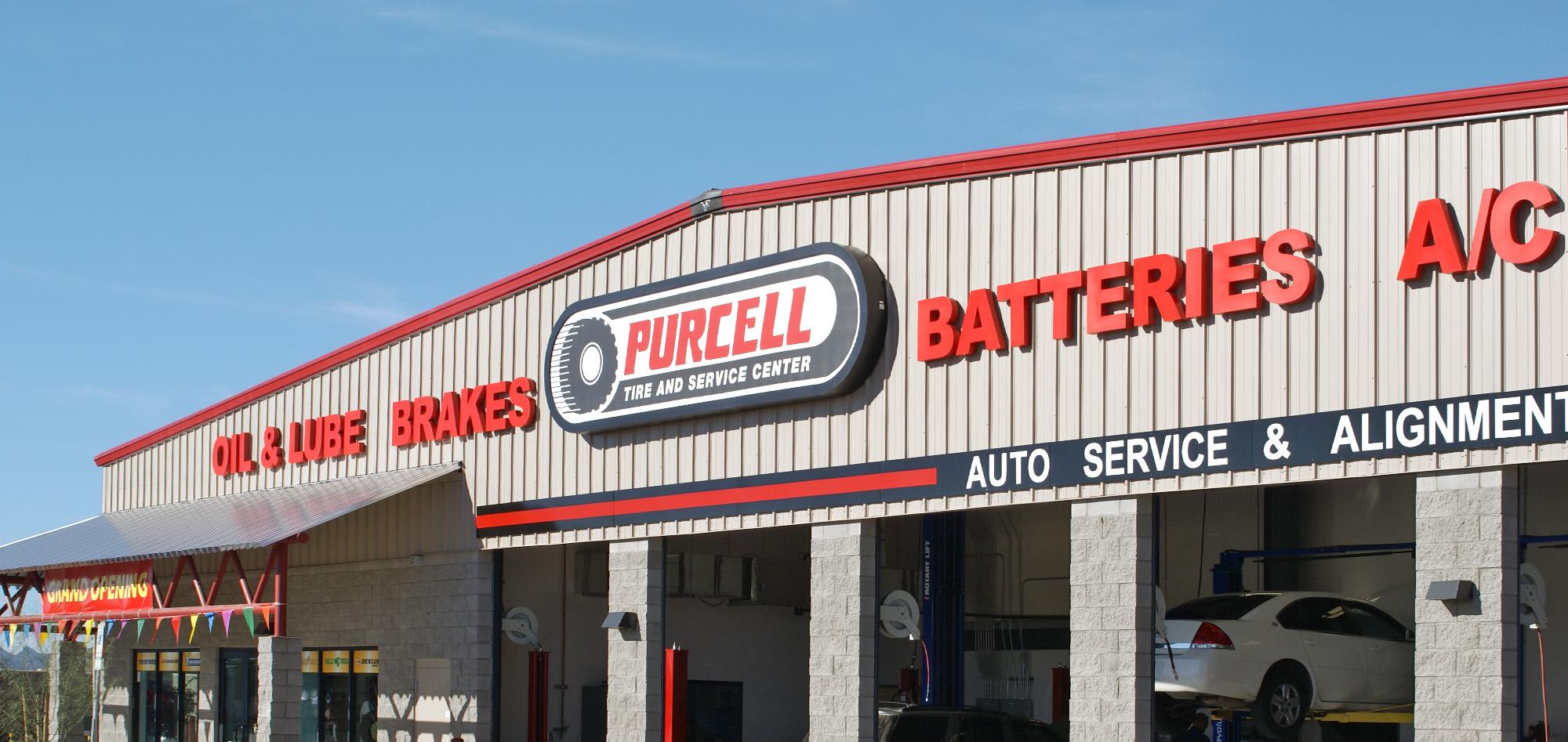 Automotive service center with red-and-gray metal facade, bold storefront signage and multiple service bays beneath a clear blue sky.