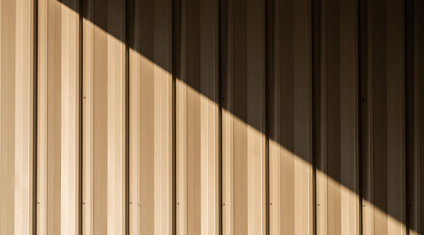 Sunlit ribbed metal wall panel with diagonal shadow