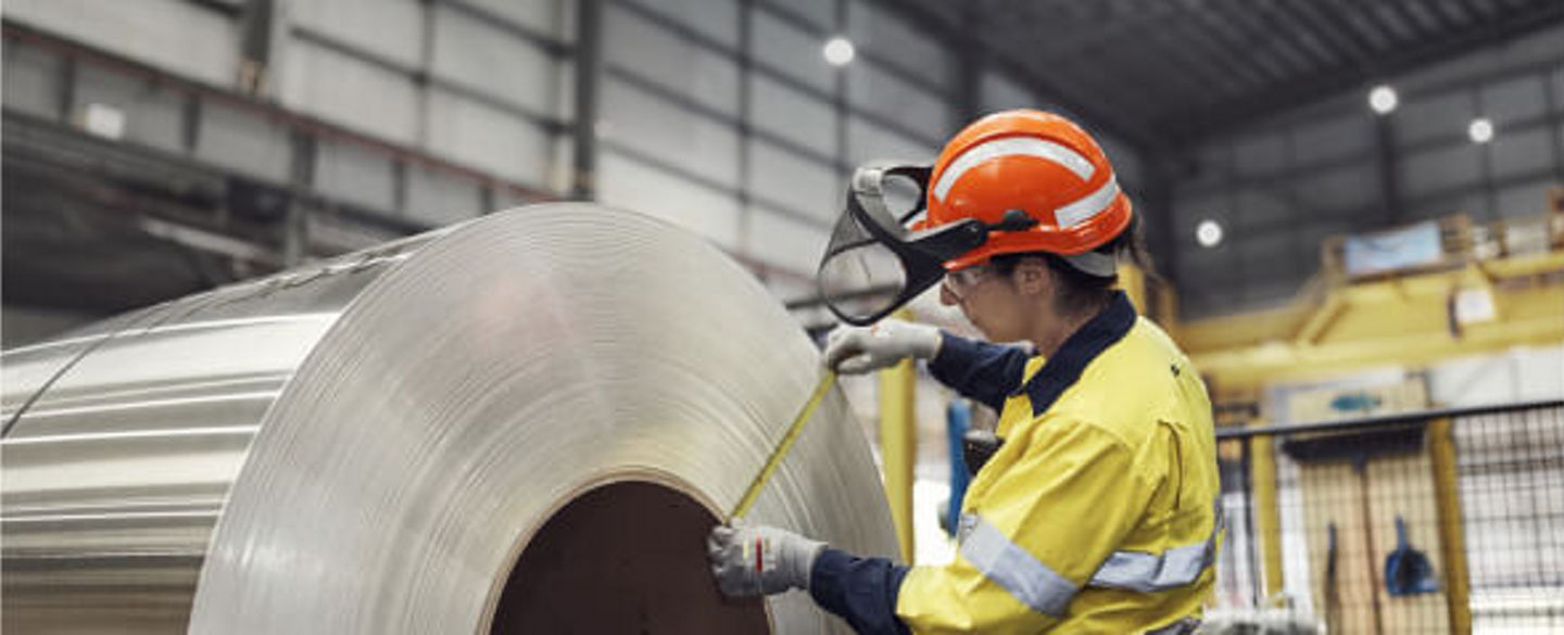 BlueScope employee in high visibility uniform with tape measure, measuring width of steel coil