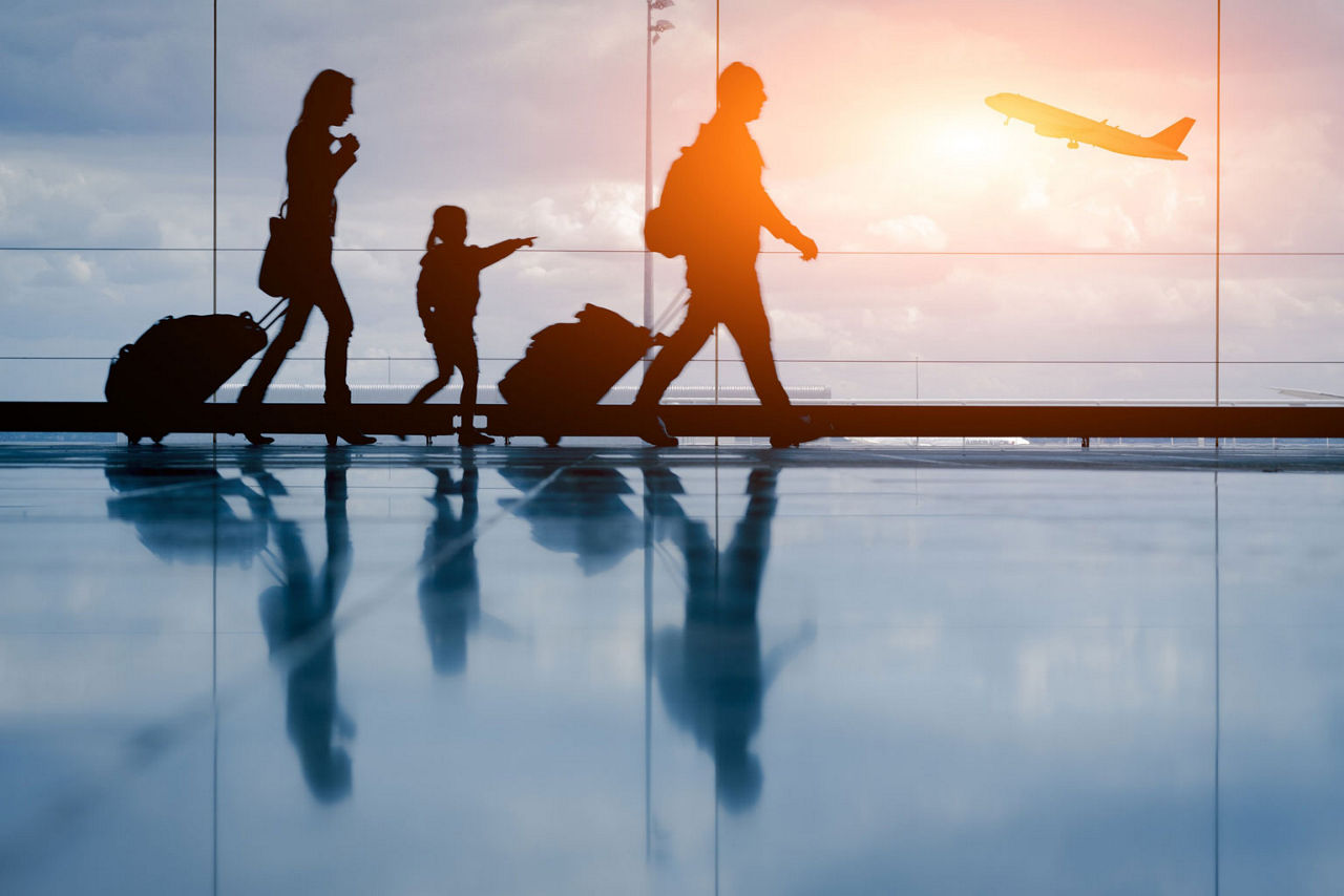 a family of travelers at an airport walking with luggage with an airplane outside the glass wall