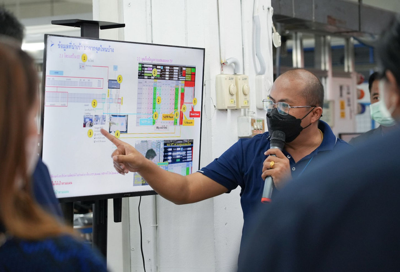 a man explaining a document on a screen in a factory to a small group standing around