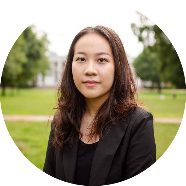 Warunya Mahavanakul portrait photo an Asian woman with long dark brown hair in a black suit and black collarless top with a lawn and a white building in the background