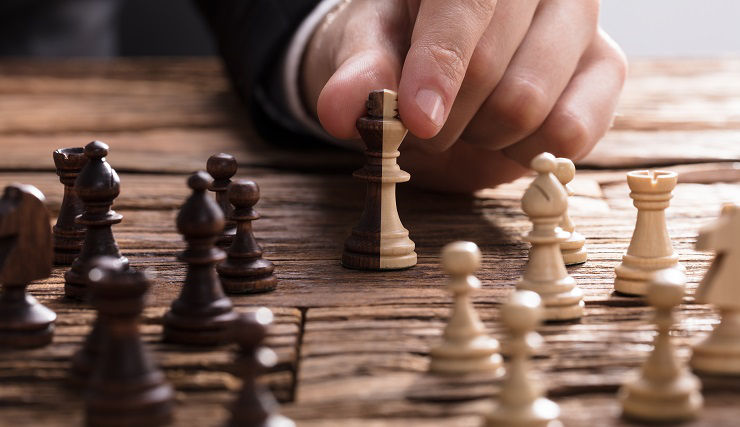 Businessperson's Hand Holding King Chess Piece On Wooden Desk