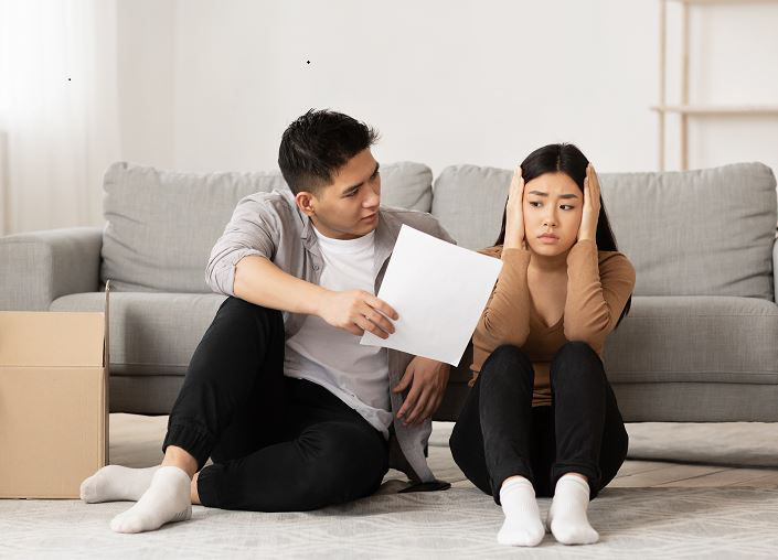 Asian Couple Forced To Sell Home Through Financial Problems, Husband Showing His Wife Eviction Notice, Sitting On Floor
