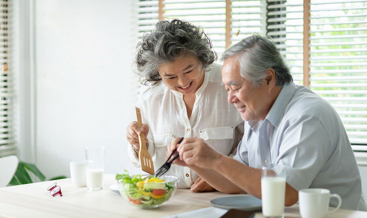 Happy Asian Older couple relaxing preparing and cooking healthy salad at home together. Romantic Senior man and woman smiling enjoying a meal. 