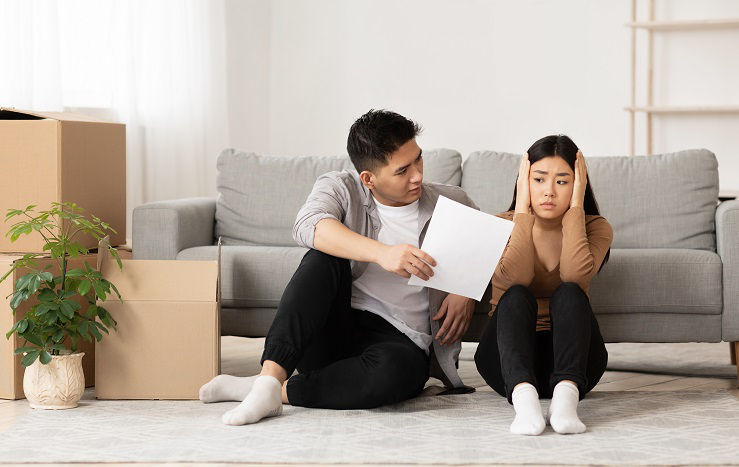 Asian Couple Forced To Sell Home Through Financial Problems, Husband Showing His Wife Eviction Notice, Sitting On Floor