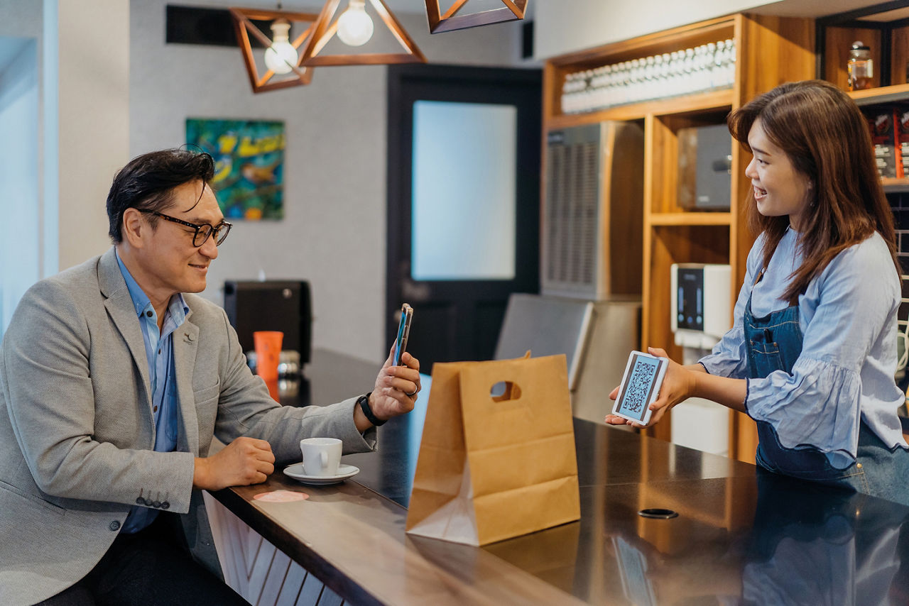 Image of an Asian Chinese man making a contactless payment with E-wallet on smartphone to cafe worker. E-wallet, mobile payment, contactless payment, cashless transaction at cafe.