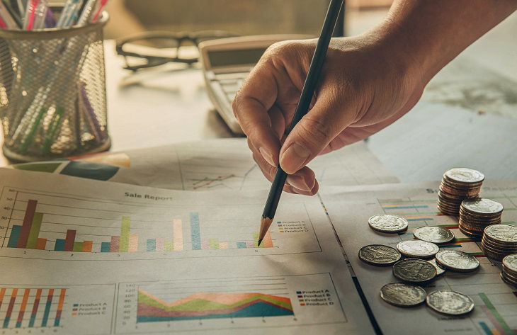 close up hand businessman holding a pencil and point summary report with thailand coin on paperwork