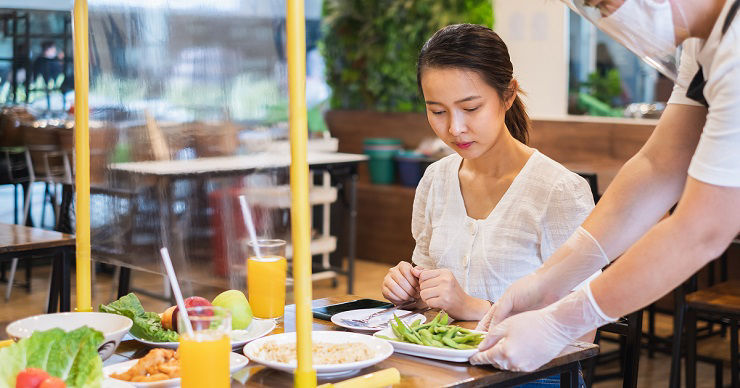 Asian woman sitting separated in restaurant eating food with table shield plastic partition to protect infection from coronavirus covid-19, restaurant and social distancing concept