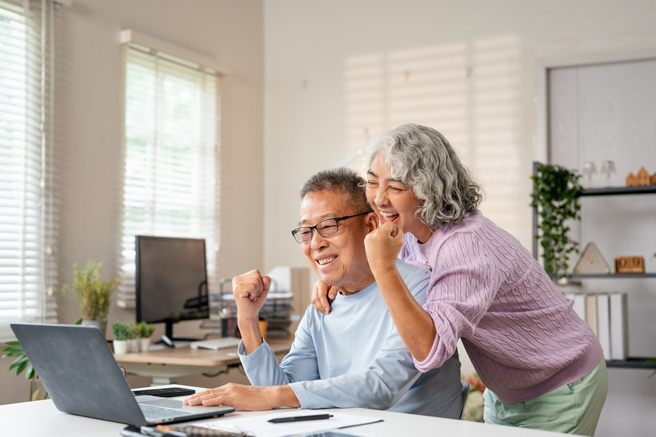 Senior married couple looking at laptop, surprised by good news, surfing internet while resting in livingroom.