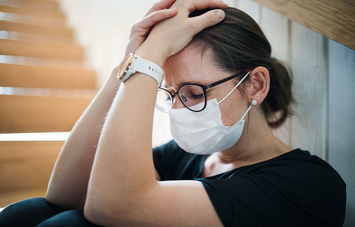 Sad woman with face mask sitting indoors at home, Corona virus and quarantine concept.