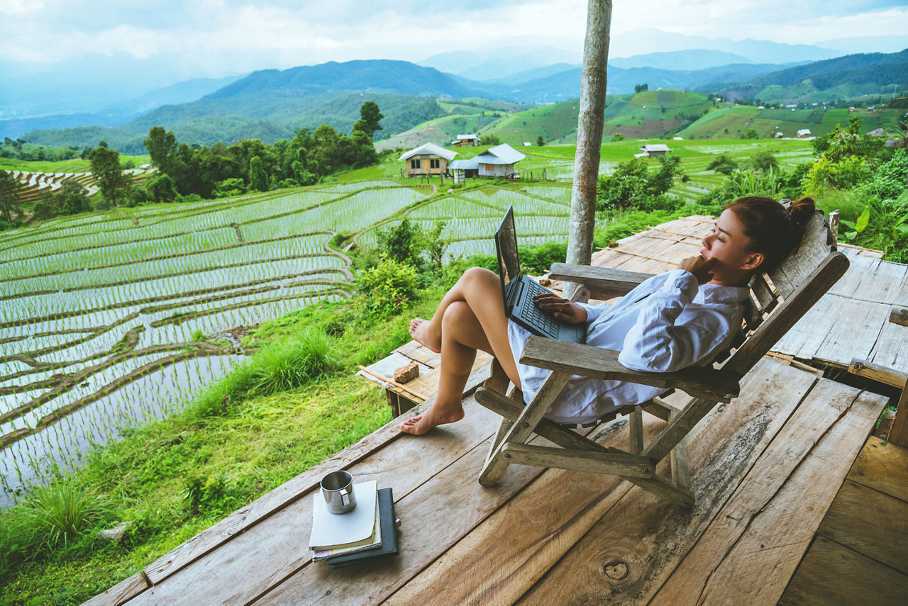 Asian woman travel nature. Travel relax. sit work with a laptop the balcony of the resort. View of the field on the Moutain in summer. Thailand