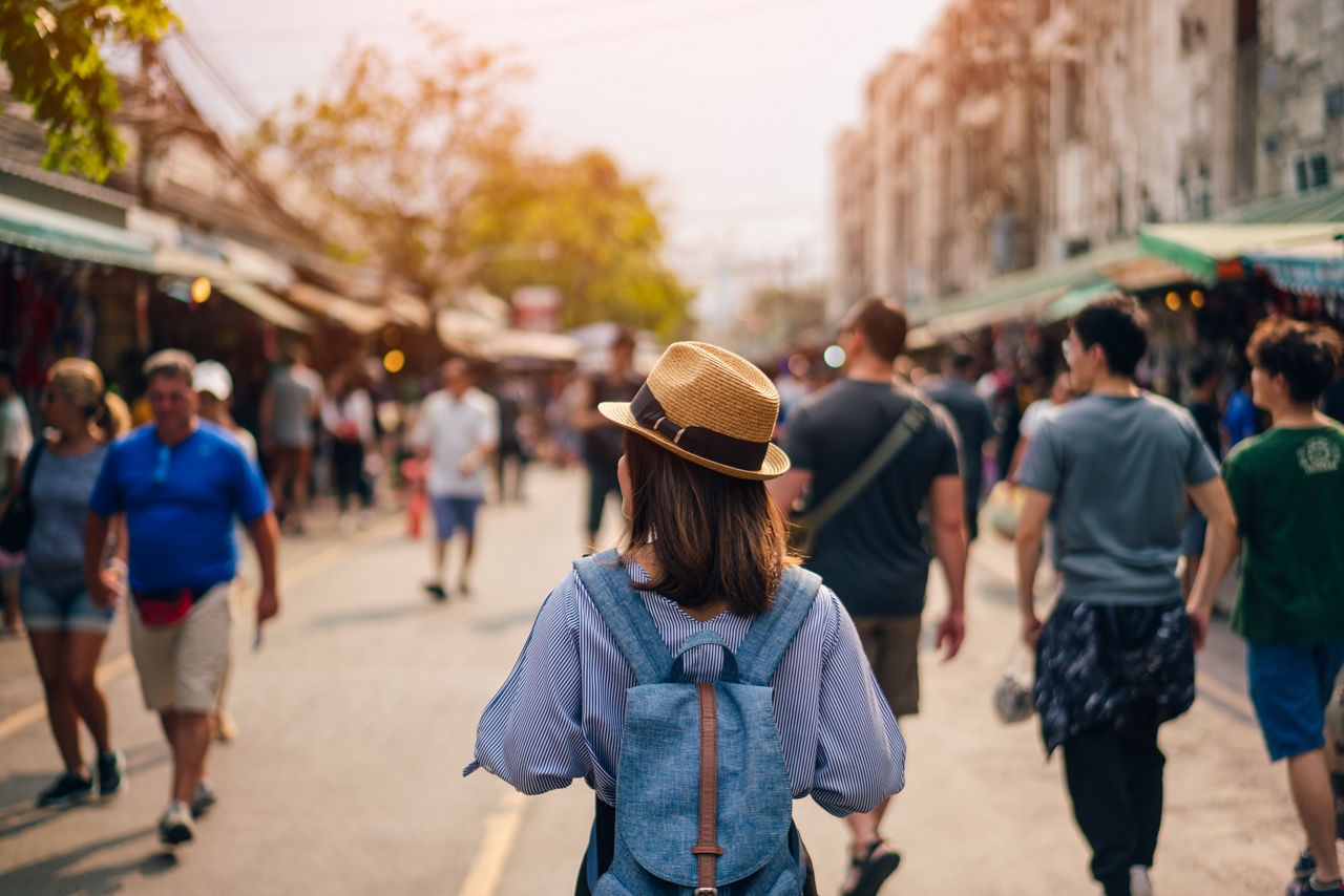 Young woman traveler with sky blue backpack and hat looking the way with in JJ Market in Bangkok Thailand. Traveling in Bangkok Thailand; Shutterstock ID 1008870292; purchase_order: BOT; job: ; client: ; other: 
