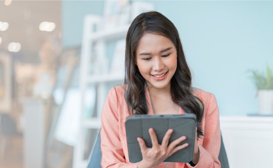 A woman on her phone looking at a tablet with a teammate working behind her