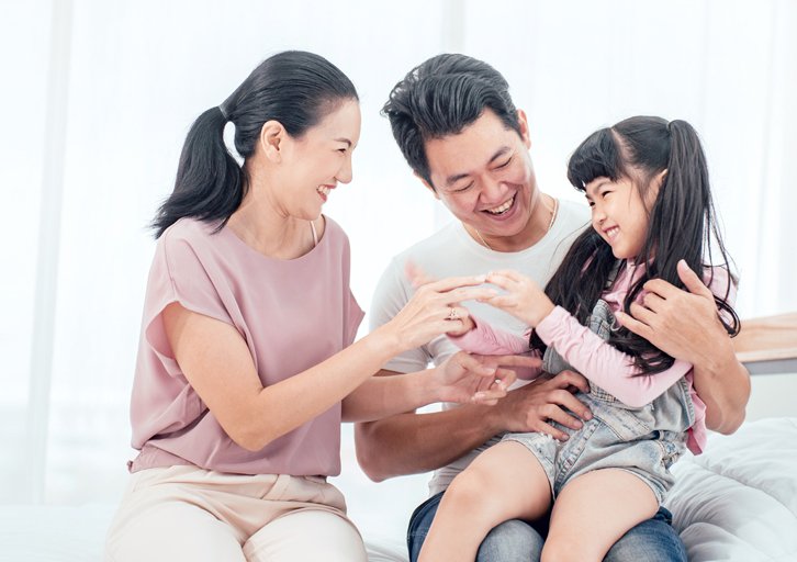 Mom, dad, and daughter all smiling and playing with each other.
