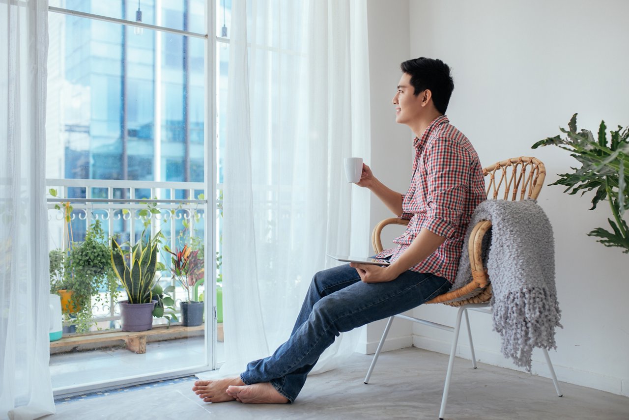 Smiling asian man drinking coffee relaxing on the couch at home