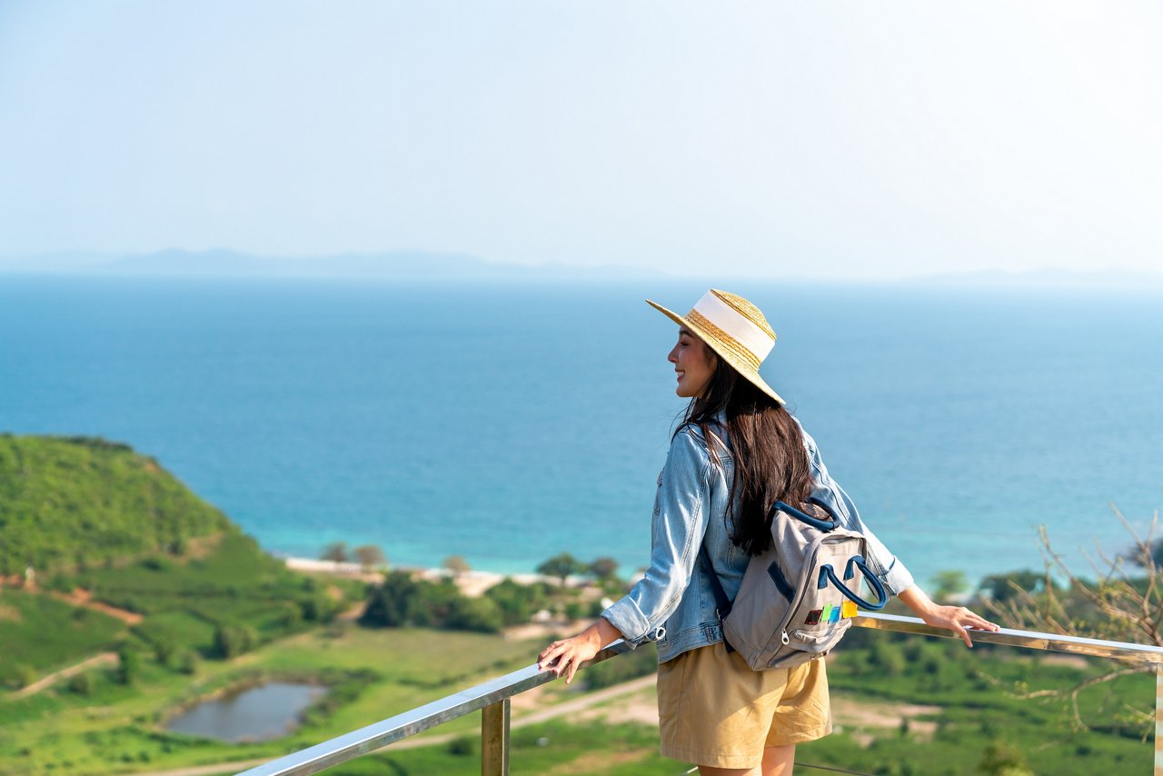 4K Young beautiful Asian woman with backpack solo travel on tropical island mountain peak in summer sunny day. Cheerful female relax and enjoy outdoor lifestyle in summer beach holiday vacation trip